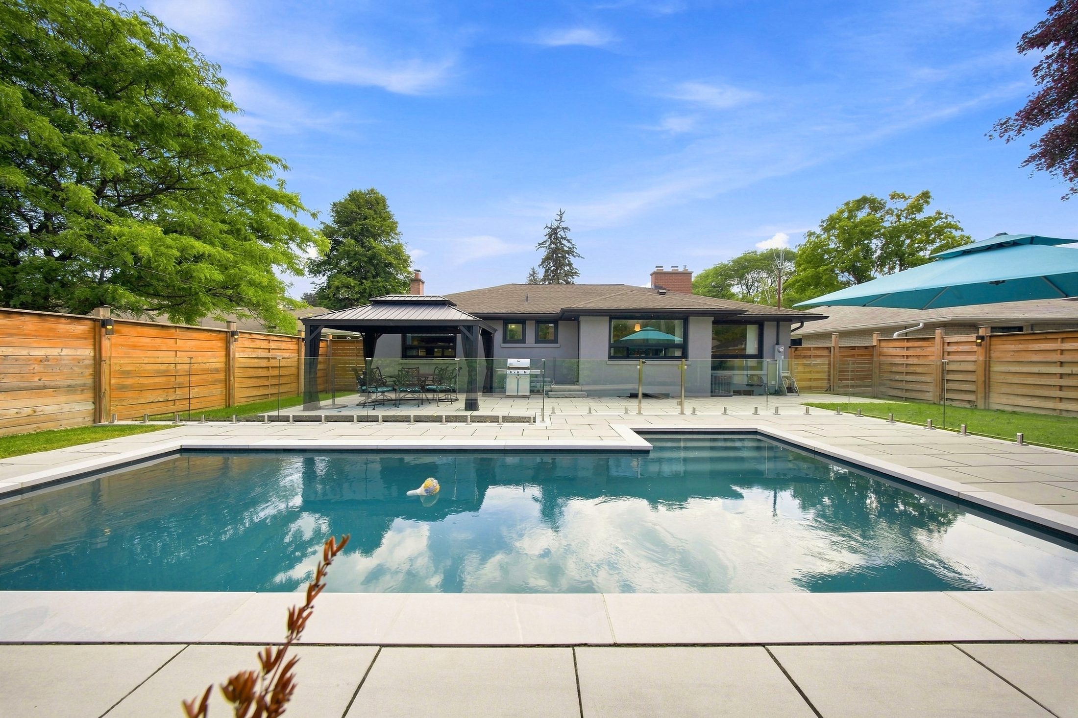 The pool, seamless glass fence and stone terrace with the house beyond