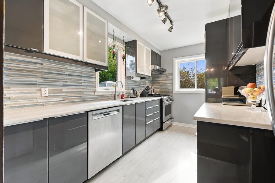 Updated galley kitchen with grey gloss cabinetry, white counters and a mosaic tile backsplash